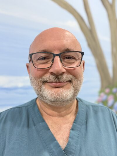 Profile photo of Dr Jammal wearing blue scrubs and reading glasses, looking at the camera with a smile.